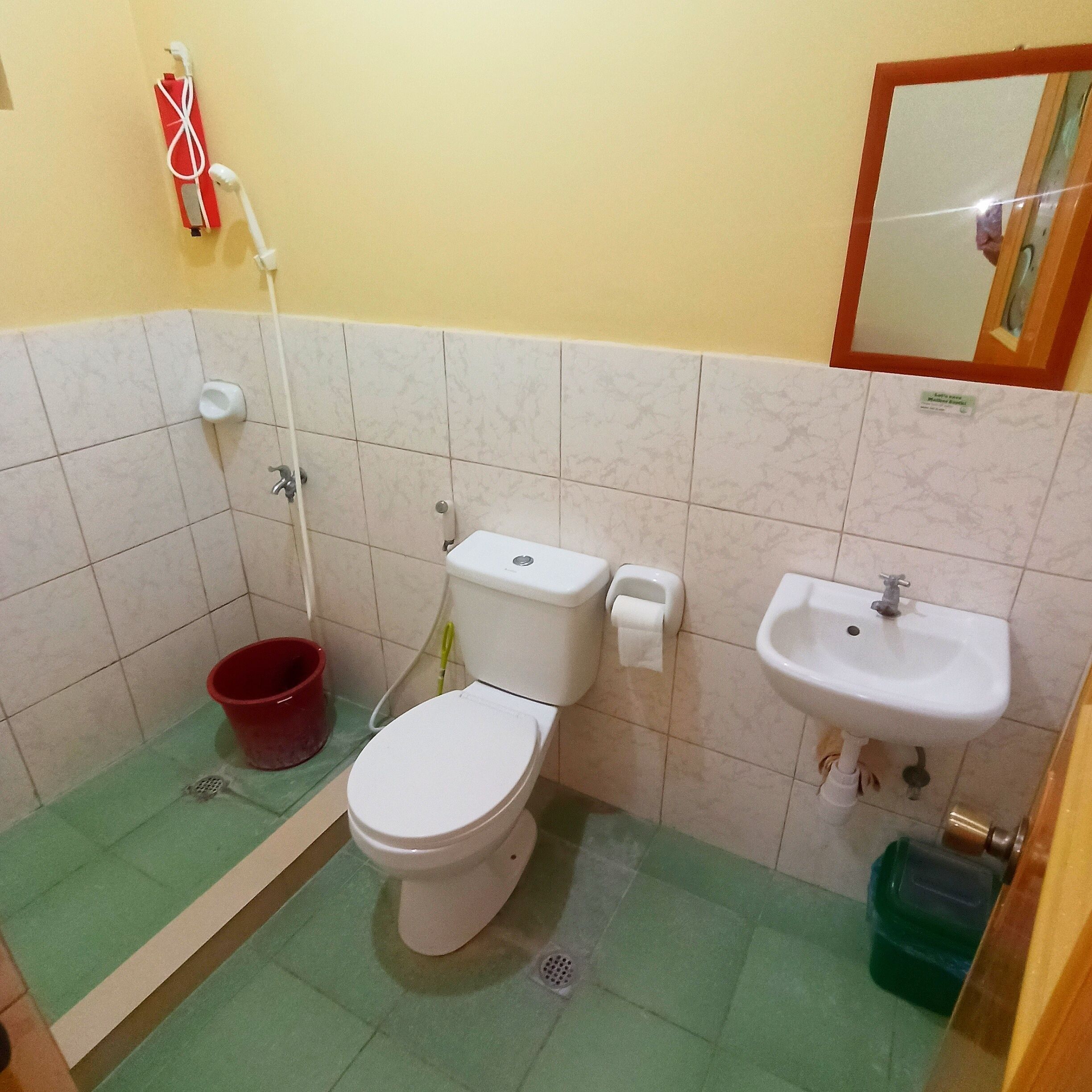 A small bathroom with a toilet, sink, and a red bucket.