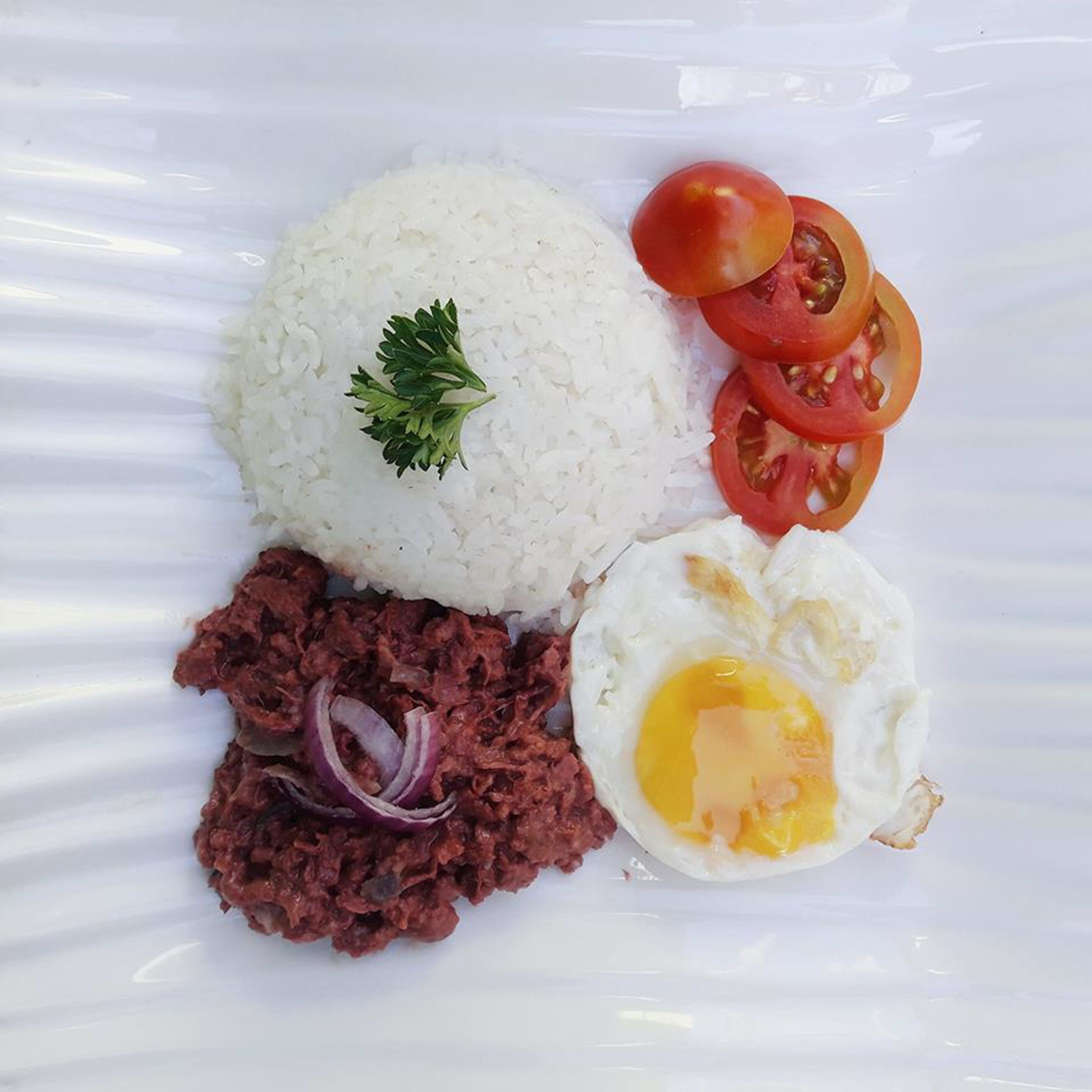 Un plato de arroz blanco cubierto de perejil, una rodaja de tomate, un trozo de cebolla roja y un huevo frito.
