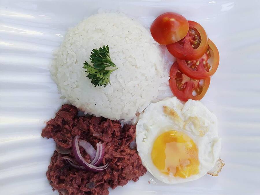 Un plato de arroz blanco cubierto de perejil, una rodaja de tomate, un trozo de cebolla roja y un huevo frito.