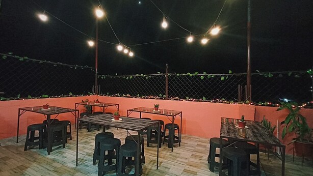 An outdoor seating area with tables and chairs, string lights overhead, and a red wall. - Pamujo Hostel (Baclayon)