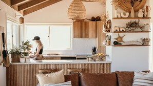 A cozy living room with a brown leather sofa, a wooden dining table, and a kitchen area with wooden cabinets and a hanging light fixture.