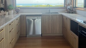A modern kitchen with wooden cabinets, a dishwasher, and a large window offering a view of the ocean.