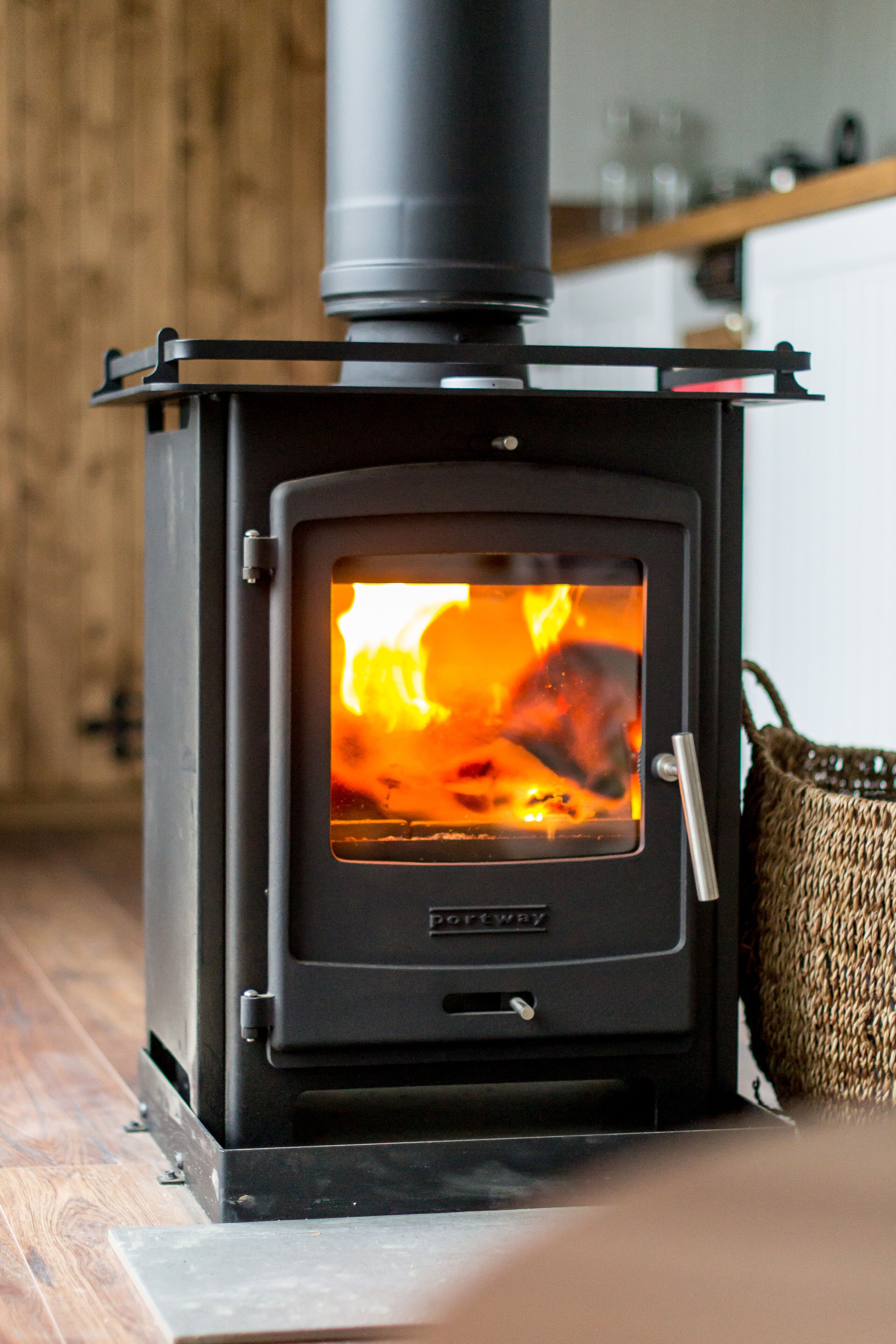 A wood-burning stove with visible flames, a metal handle, and a brand name "Porthway" on the front.