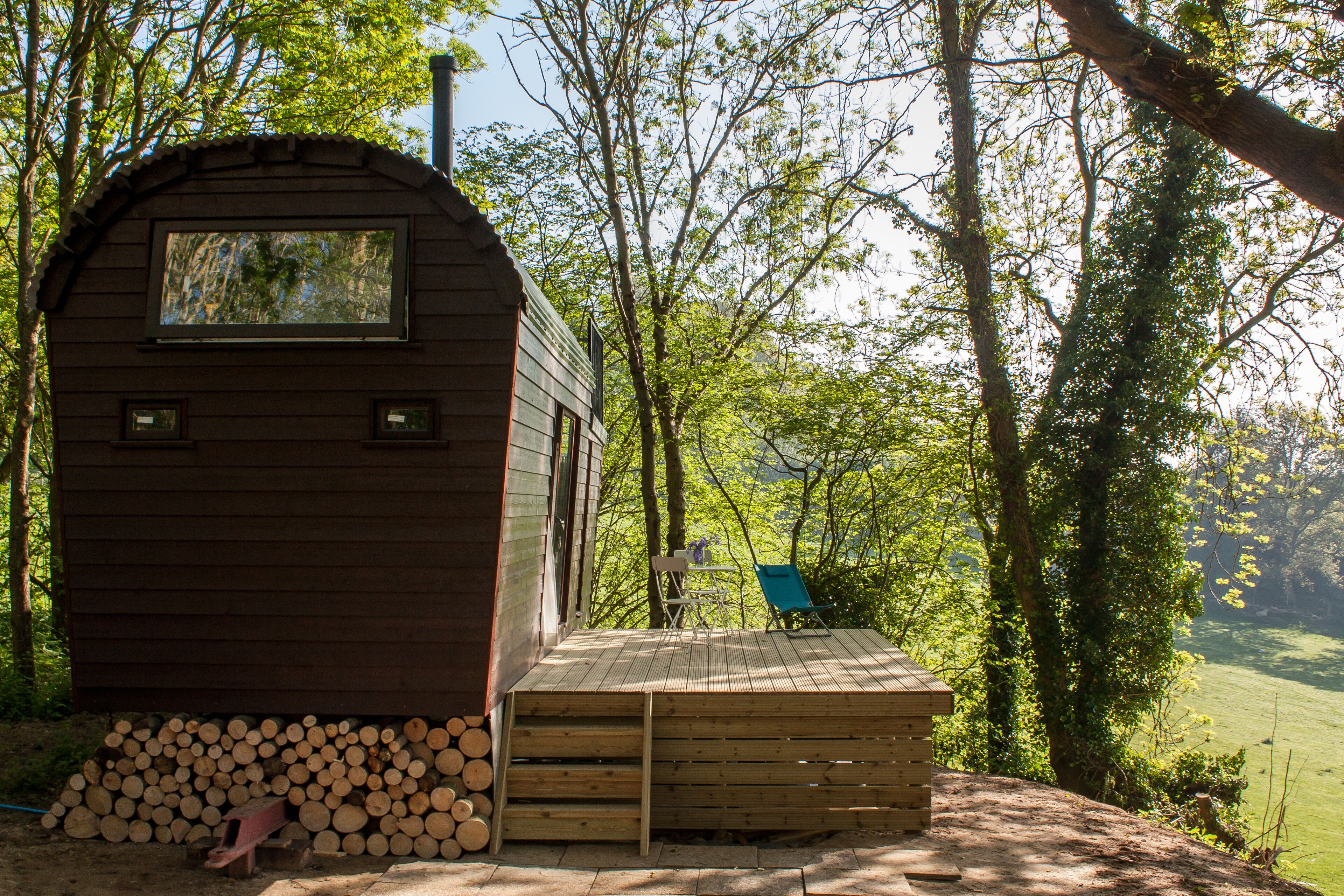 Une cabane en bois dotée d’une terrasse, entourée d’arbres et offrant une vue sur un paysage verdoyant.