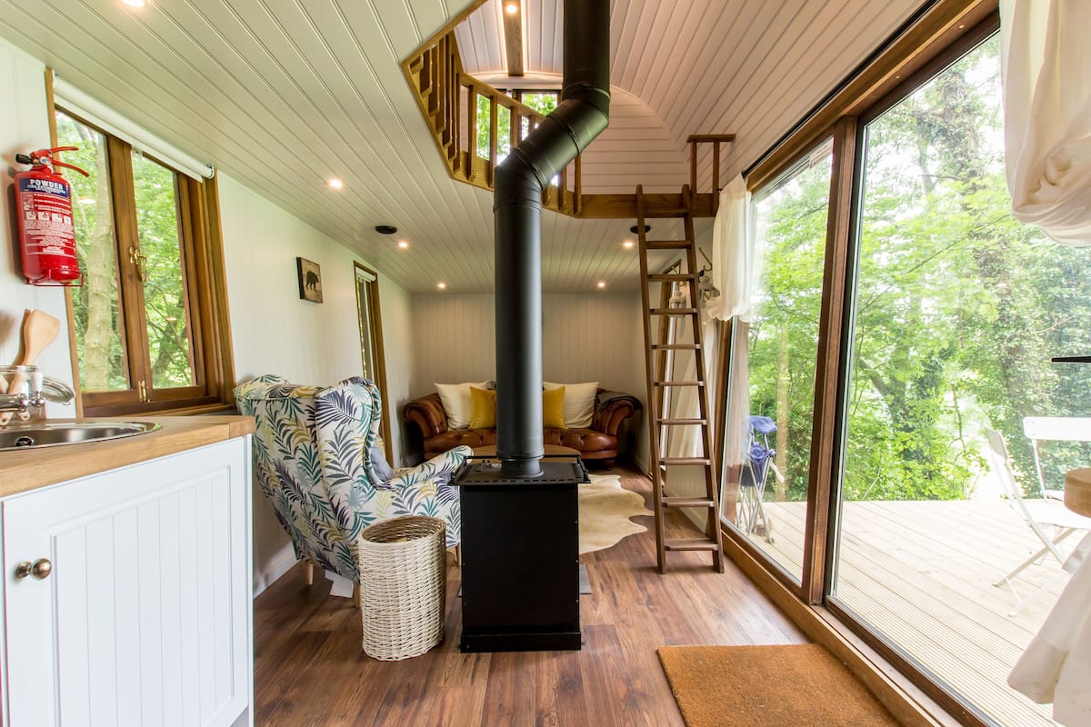 A cozy interior with a wood-burning stove, a kitchen area, a sofa, and a view of the outdoors.