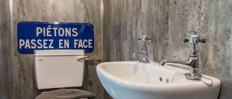 Une salle de bain avec des toilettes, un lavabo et un panneau bleu sur lequel on peut lire : « PIÉTONS, PASSEZ DE L’AUTRE CÔTÉ ».