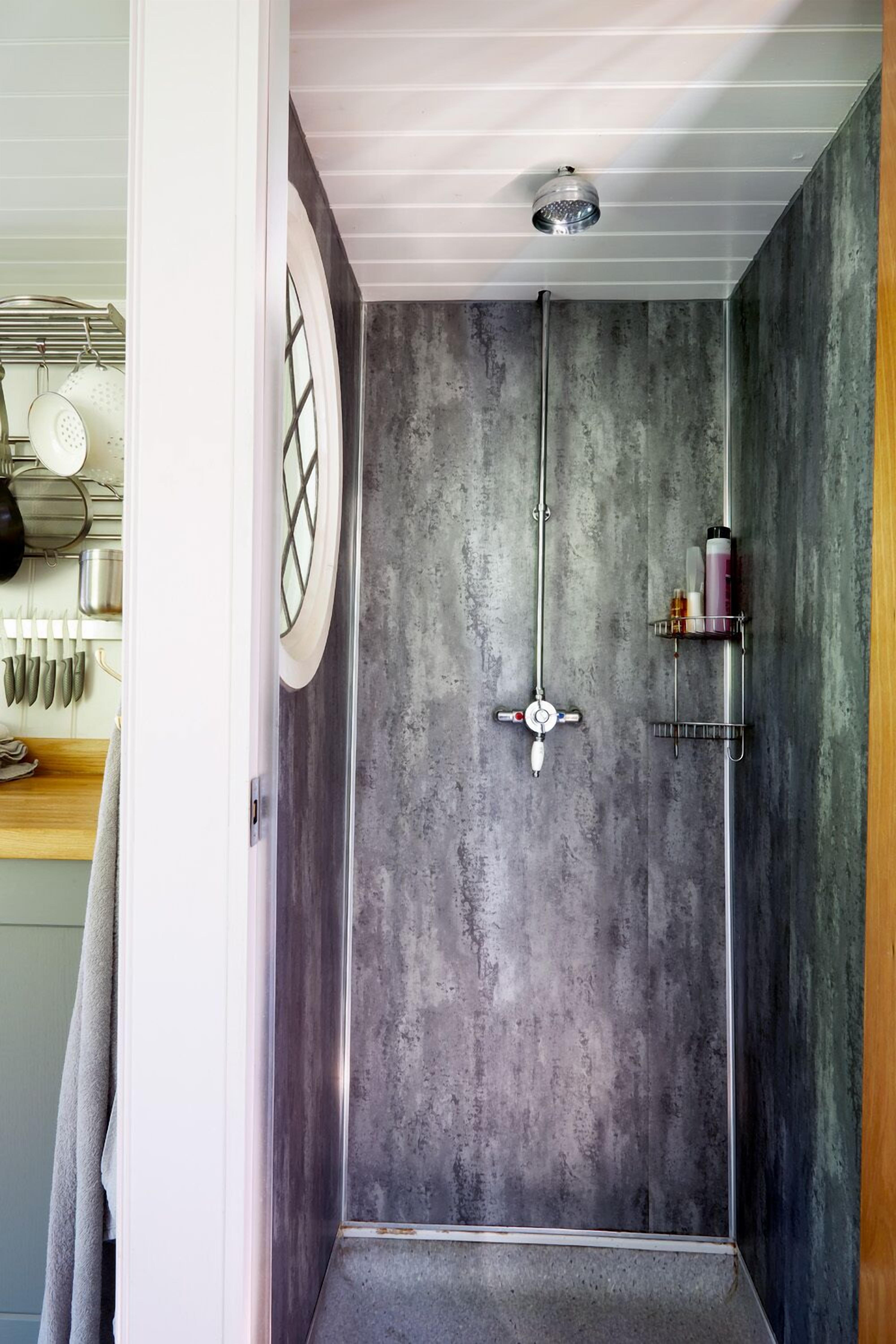 A shower with a concrete wall, a ceiling light, and a shelf with toiletries.