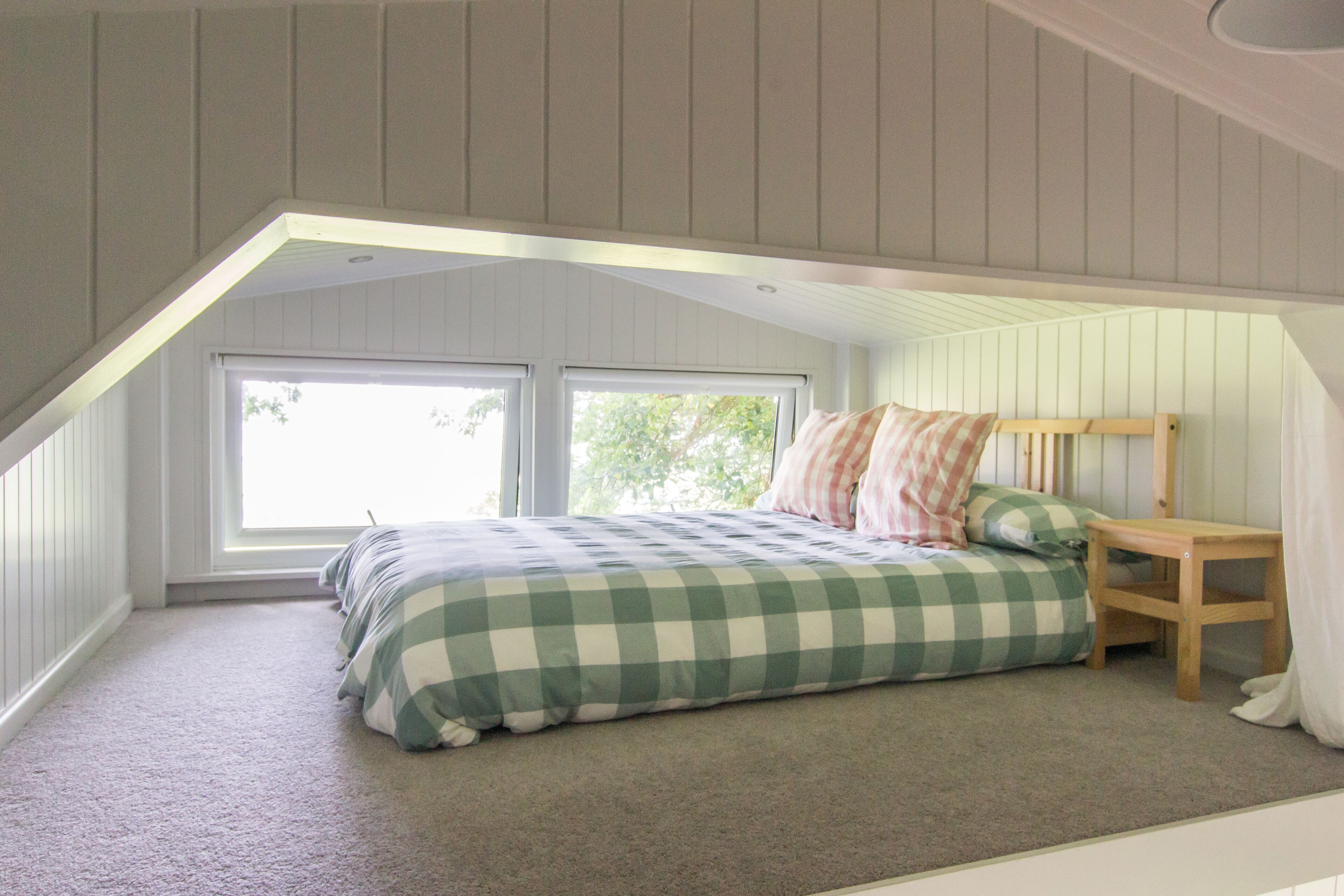 A bedroom with a sloped ceiling, a bed with checkered bedding, two windows, and a small wooden nightstand.