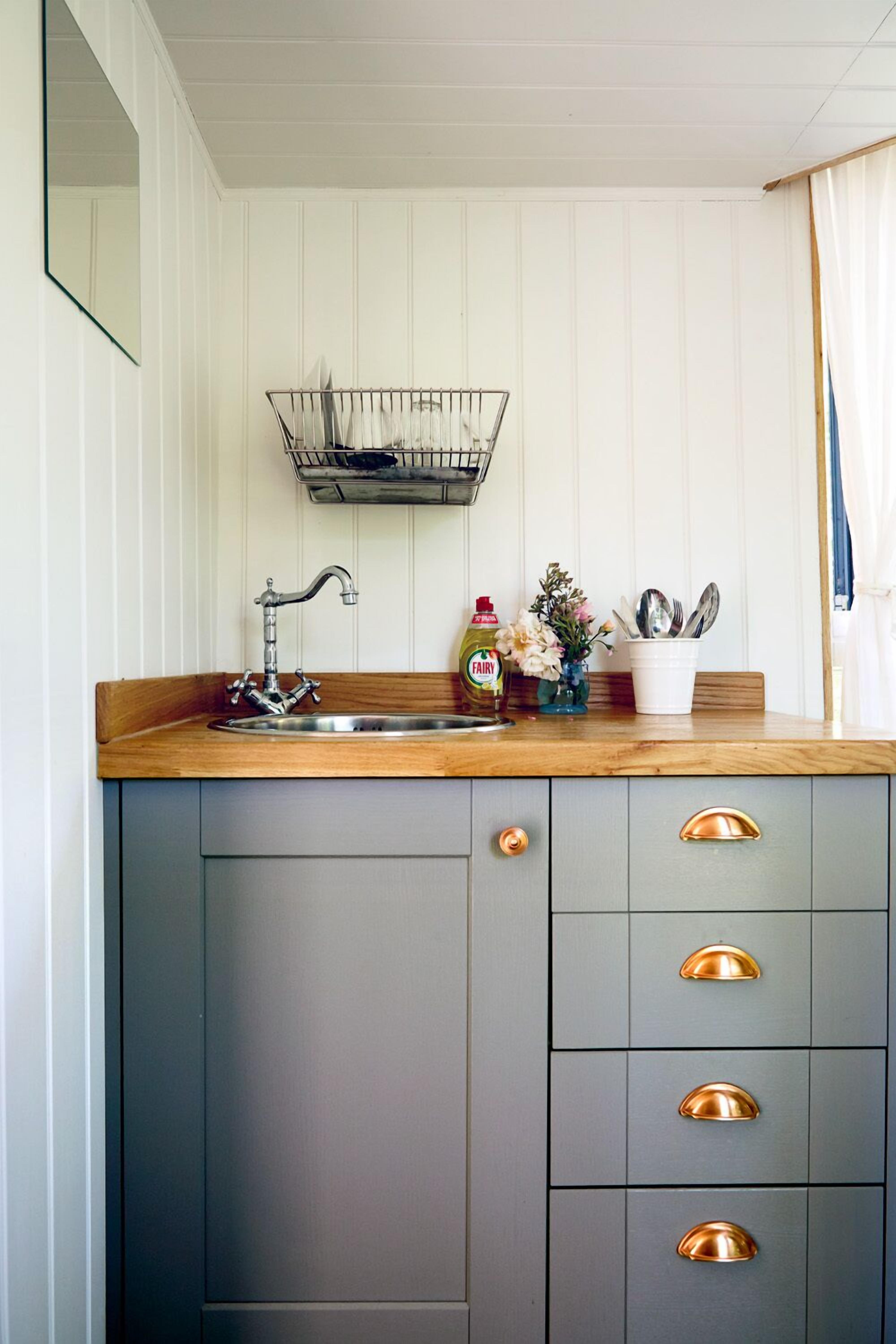 A kitchen with a wooden countertop, a stainless steel sink, and a built-in cabinet with gold handles.