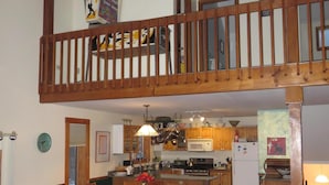 A spacious living area with a high ceiling, a wooden staircase, a dining area with a brown leather sofa, and a kitchen with wooden cabinets and modern appliances. - Franconia Notch Retreat, Huge Views, Hot Tub, EV charger, A/C (Sugar Hill)