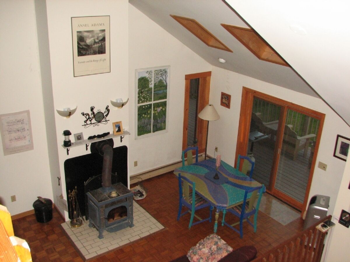 Una sala de estar acogedora con una estufa de leña, una mesa de comedor con sillas y un ventanal con vistas al follaje.