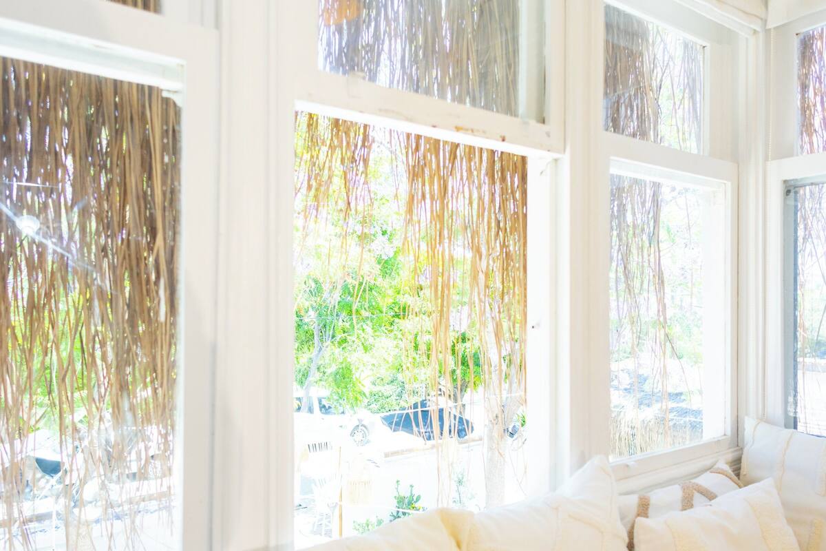 A room with a large bed, white bedding, and multiple windows with sheer curtains.