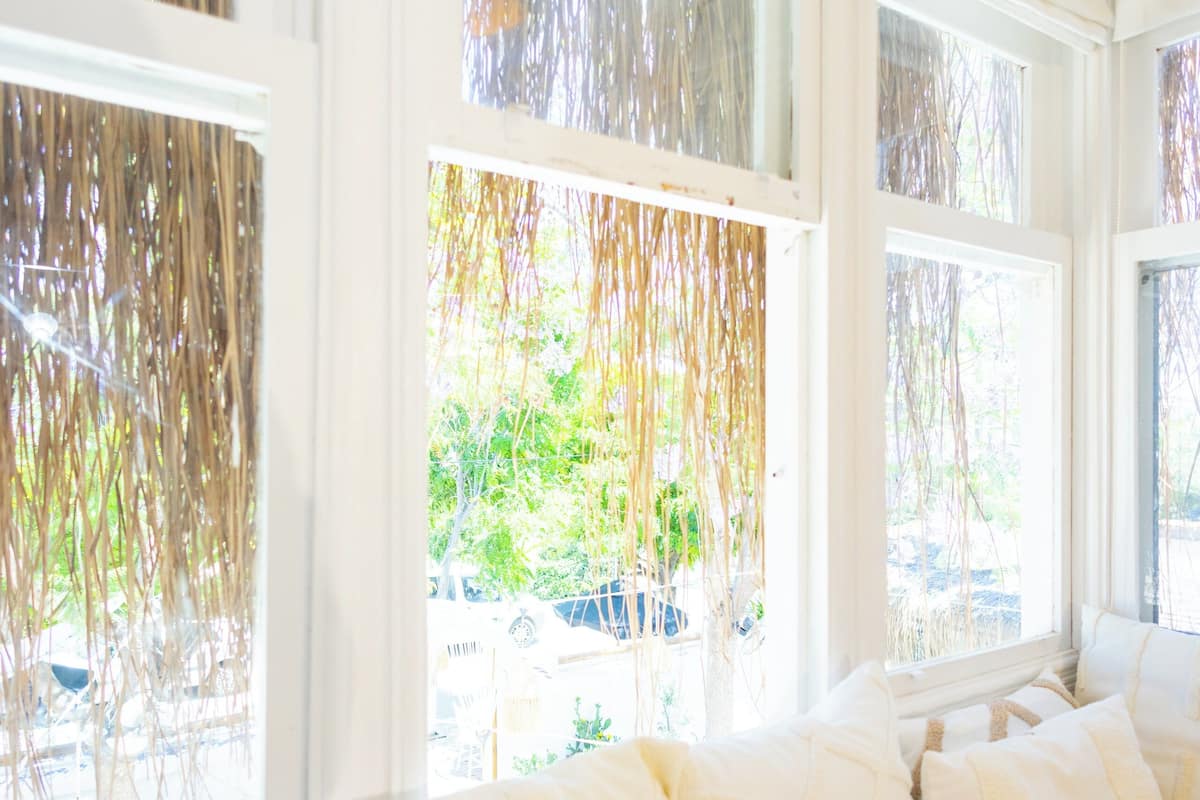 A room with a large bed, white bedding, and multiple windows with sheer curtains.
