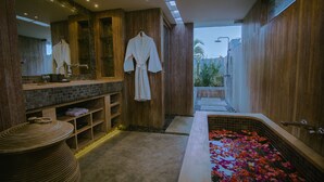 Ein modernes Badezimmer mit Holzvertäfelung, einer großen Badewanne mit Rosenblüten, einem Spiegel und einem Handtuchhalter.