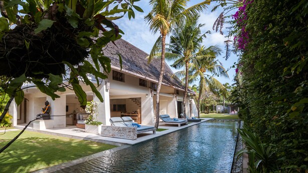 Ein Poolbereich mit Liegestühlen, ein Haus mit einem Strohdach und üppige Bepflanzung.