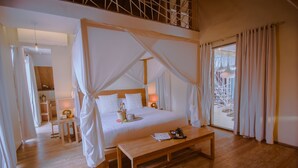 Ein Schlafzimmer mit Himmelbett, einem hölzernen Nachttisch, einem Beistelltisch und Blick ins Freie durch ein großes Fenster.