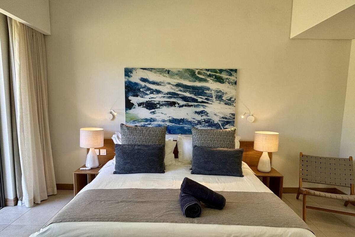 Ein Hotelzimmer mit einem großen Bett, zwei Nachttischen mit Lampen, einem großen abstrakten Gemälde an der Wand und einem Sessel in der Ecke.
