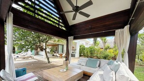 A covered outdoor seating area with a wooden floor, a sofa with cushions, a coffee table, and a ceiling fan. - Mont Choisy Le Parc by Pam Golding (Mont Choisy)