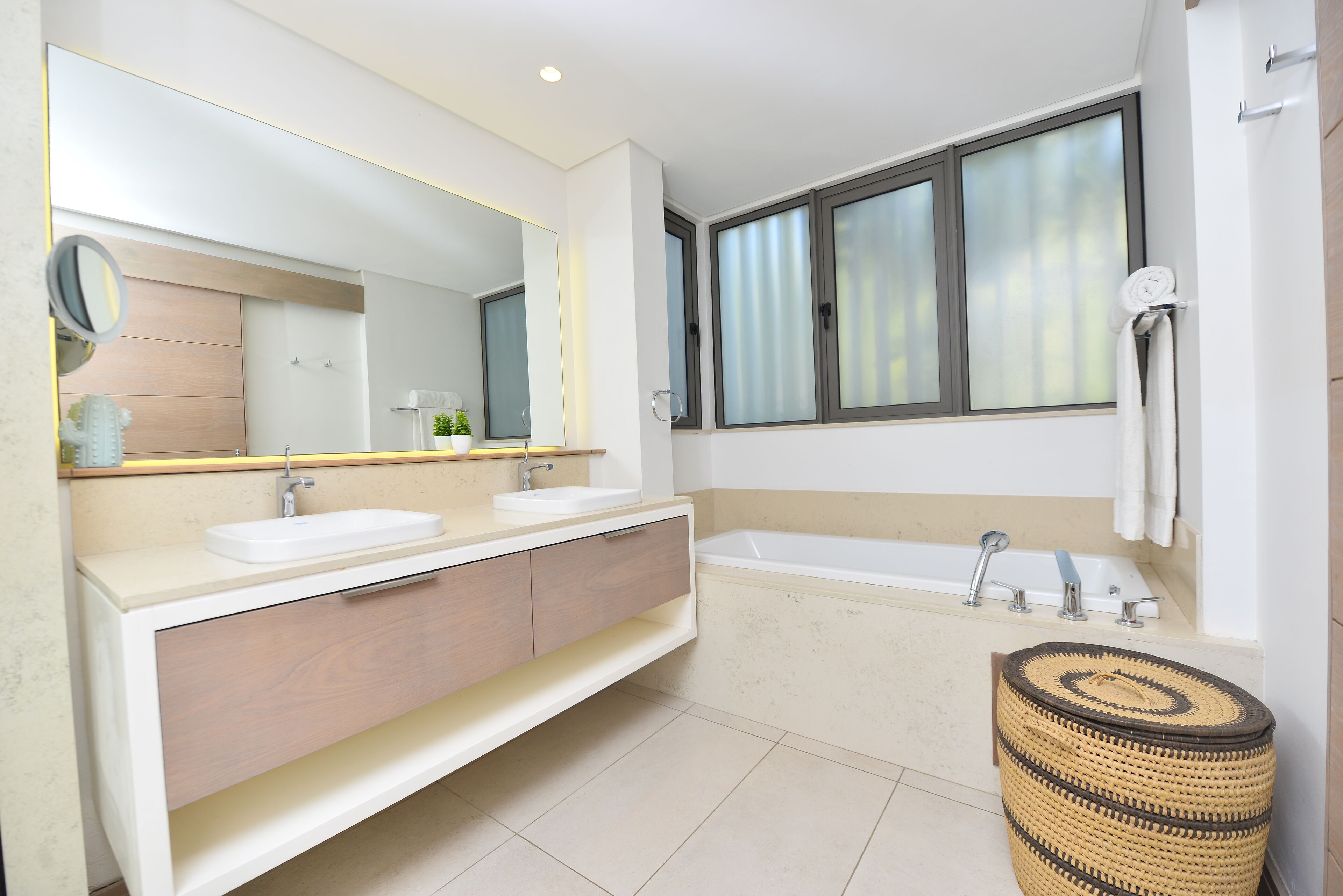 Une salle de bain moderne avec un meuble-lavabo à deux vasques, un grand miroir, une baignoire et une fenêtre en verre dépoli.