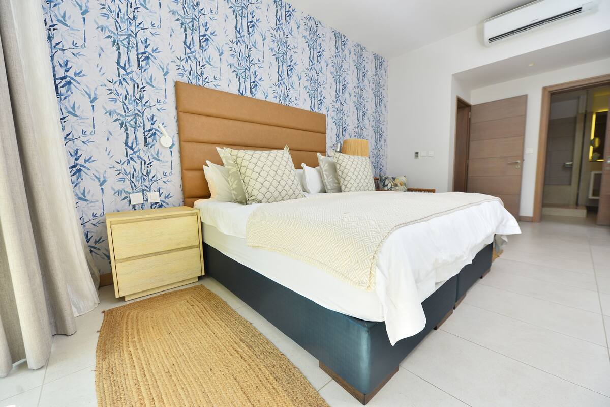 Ein Schlafzimmer mit Bett, Nachttischen, einem Holz-Kopfteil und einer Wand mit Muster.