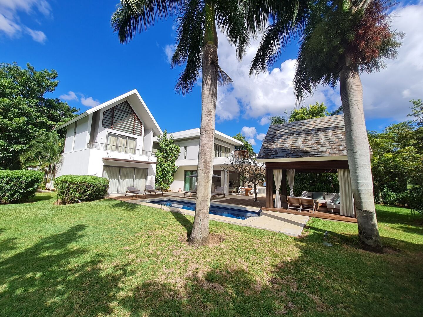 A modern two-story house with a swimming pool, surrounded by well-maintained lawns and palm trees.