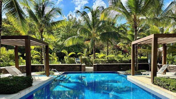 A swimming pool with clear blue water, surrounded by lush greenery and palm trees. - Mont Choisy Le Parc by Pam Golding (Mont Choisy)