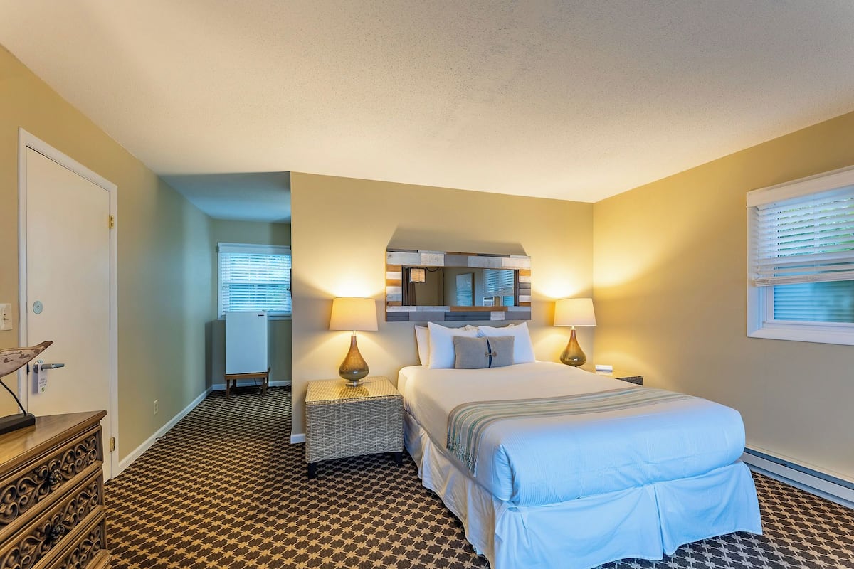A hotel room with a bed, two bedside tables, a mirror, and a patterned carpet.