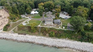 An aerial view of a residential area with houses, a white tent-like structure, and a rocky shoreline.