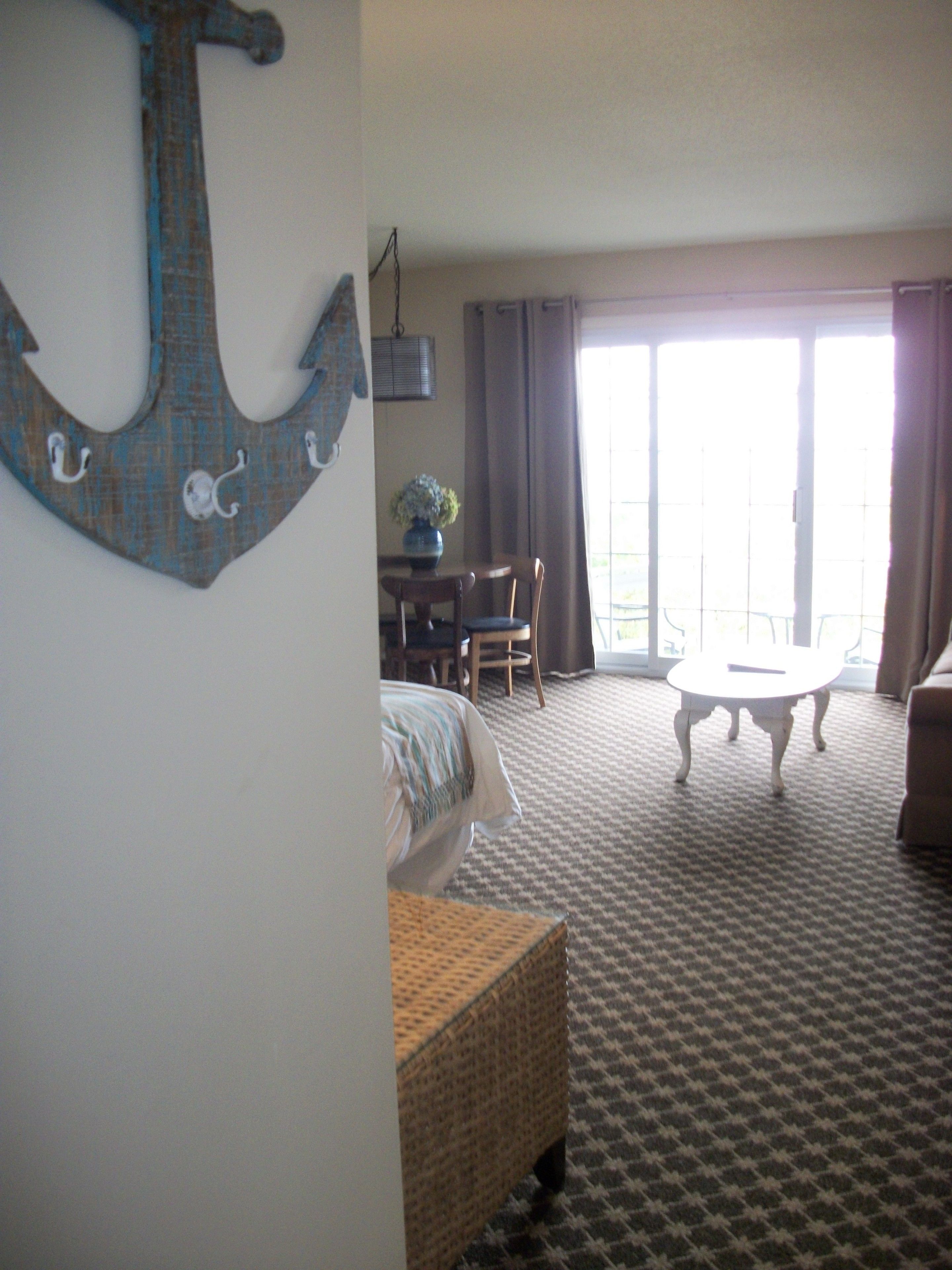 Ein Hotelzimmer mit einem Bett, einem Esstisch und einem Stuhl. Ein großes Fenster mit Vorhängen ist vorhanden.