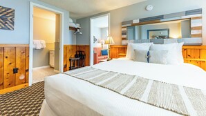 A hotel room with a bed, a desk, a chair, a lamp, and a mirror.