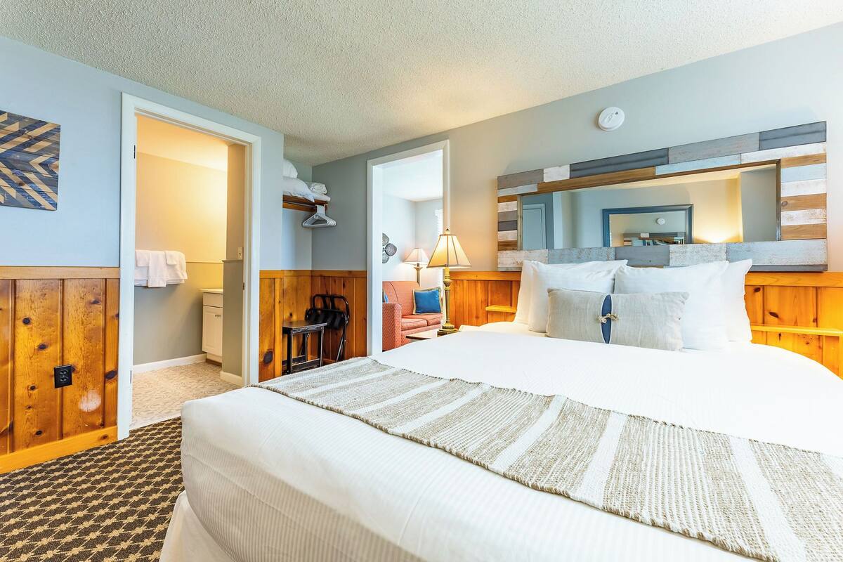 A hotel room with a bed, a desk, a chair, a lamp, and a mirror.