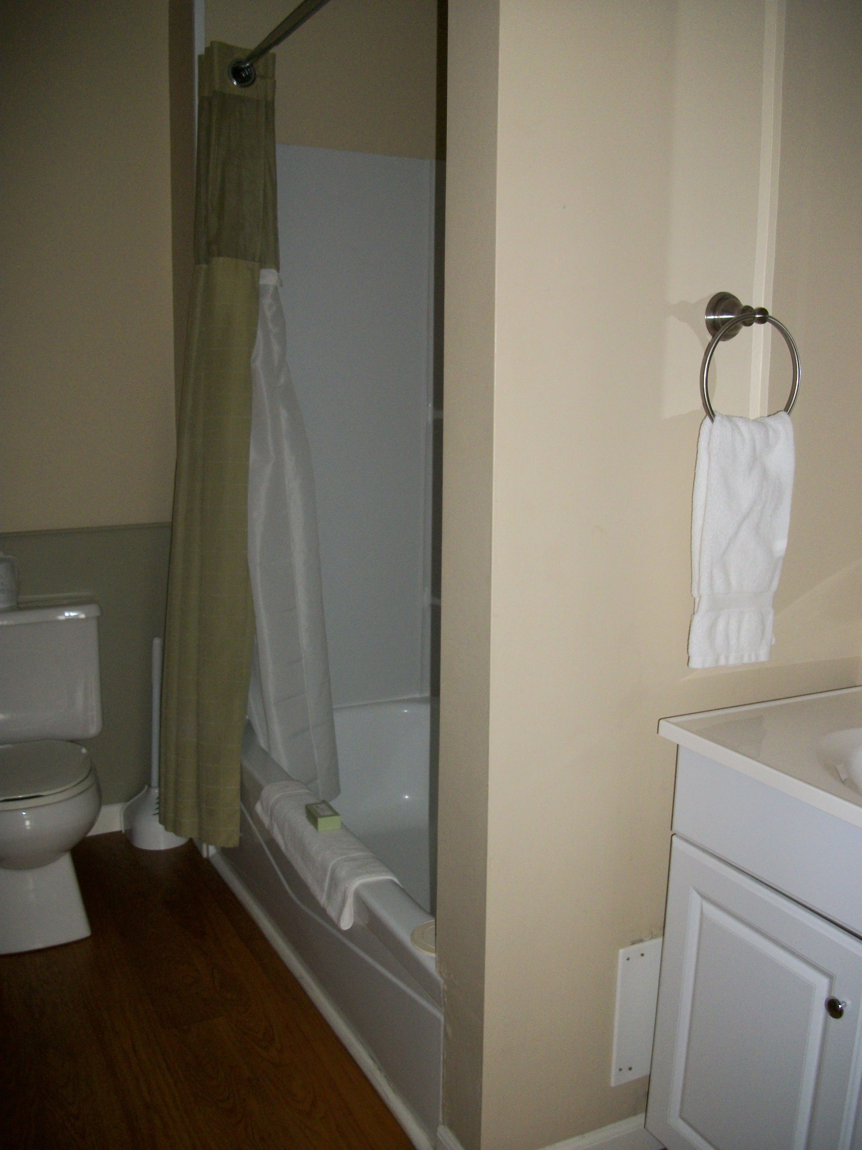 A bathroom with a toilet, a shower with a curtain, a sink, and a towel rack.