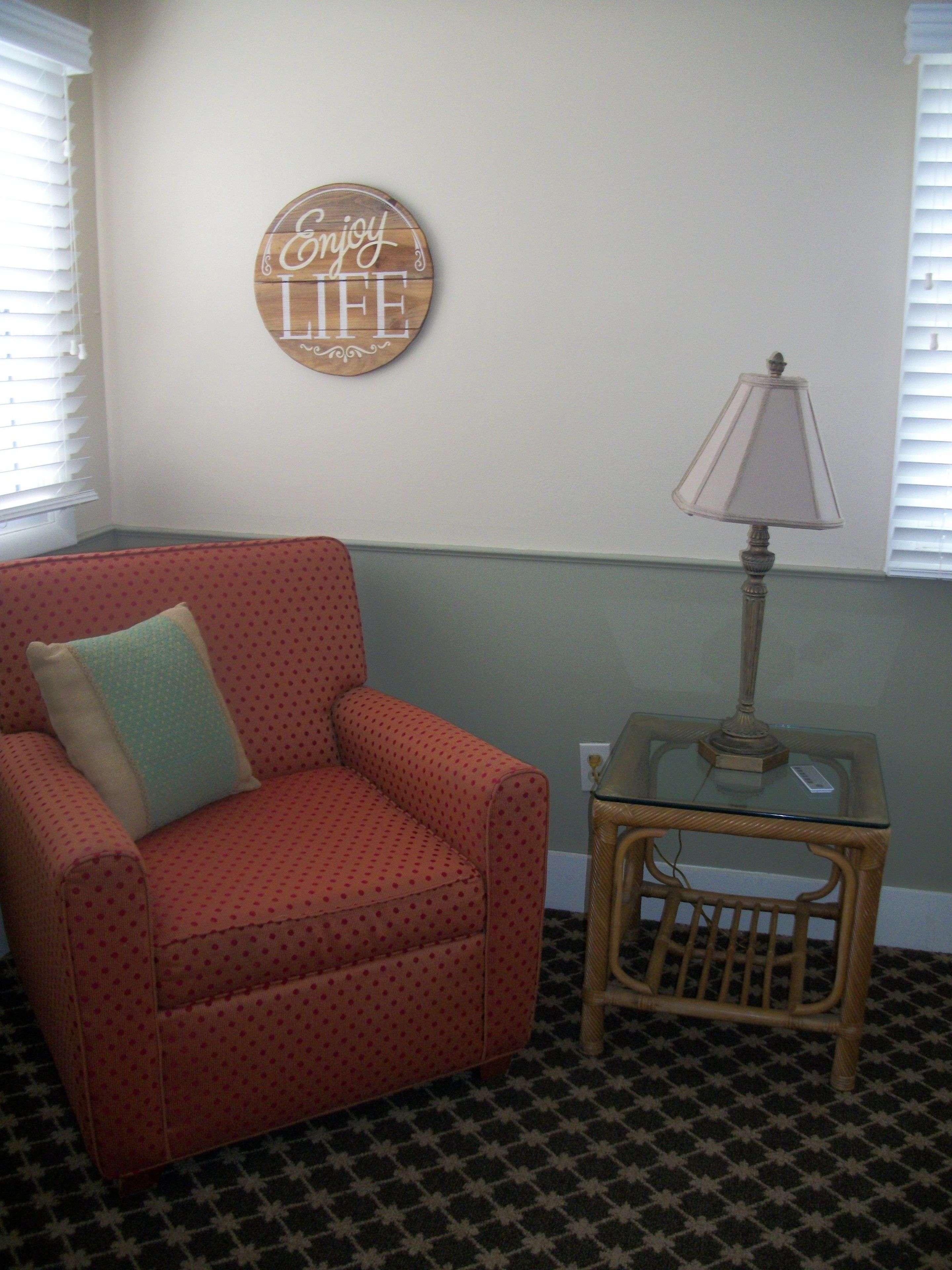 A room with a polka-dotted armchair, a small table with a lamp, and a wall sign that says "Enjoy Life".