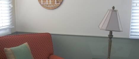 A room with a polka-dotted armchair, a small table with a lamp, and a wall sign that says "Enjoy Life".