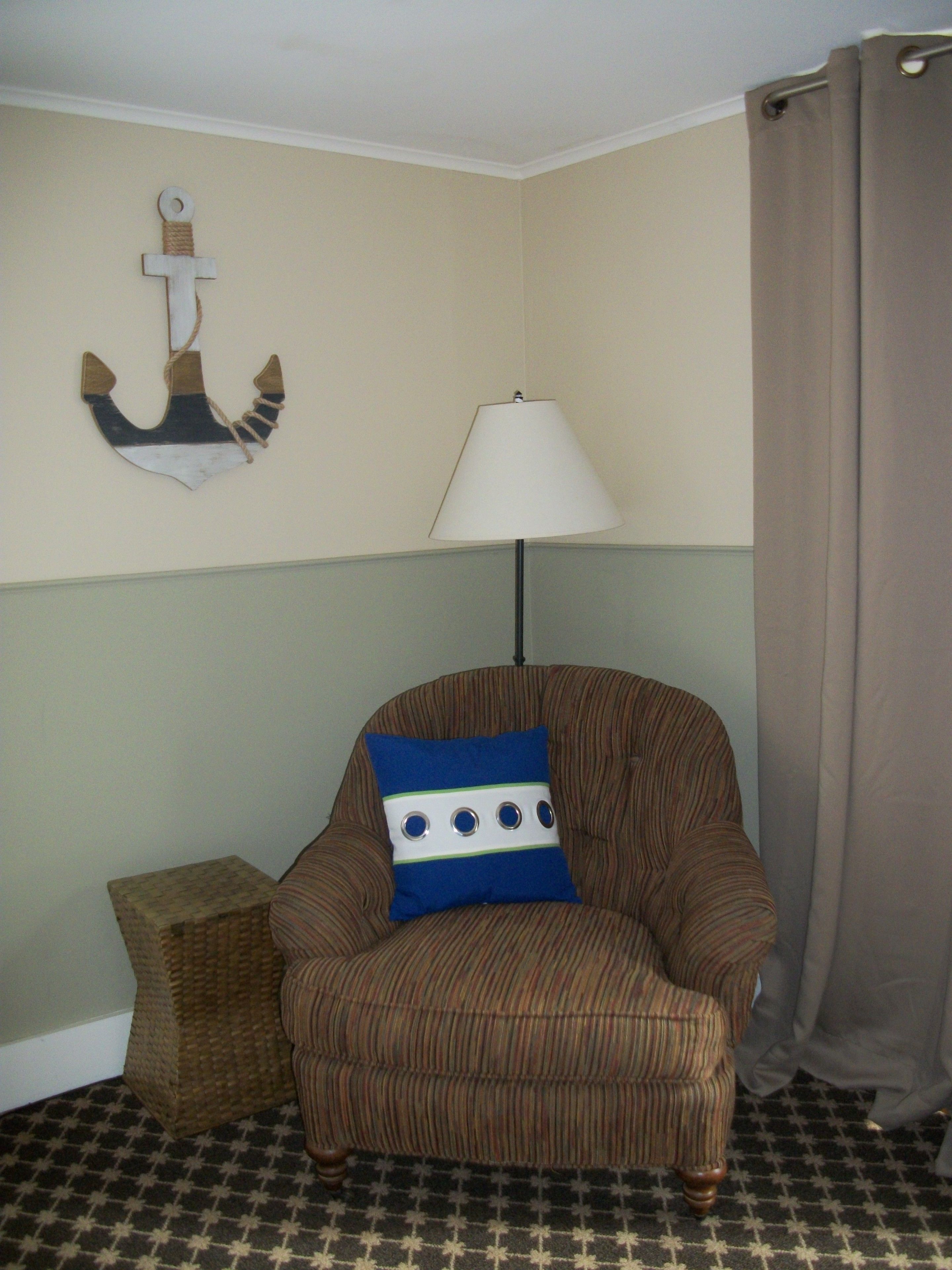 A corner room with a striped armchair, a small side table, a lamp, and a wall anchor decoration.