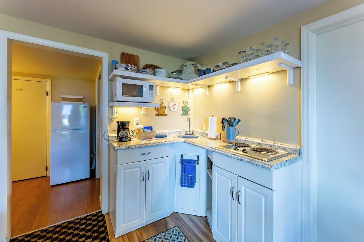 A compact kitchen with white cabinets, a microwave, a coffee maker, and a gas stove.