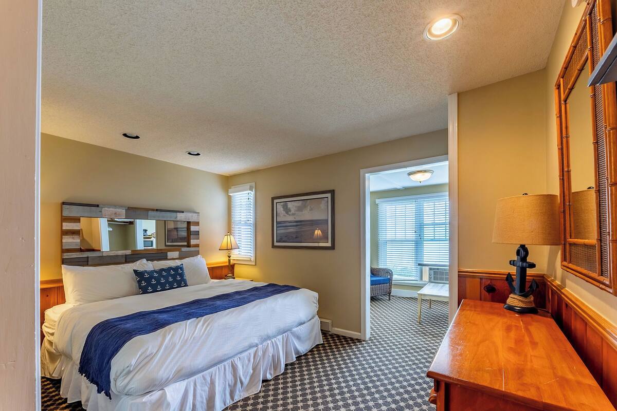 A hotel room with a bed, a desk, a lamp, a picture on the wall, and a window.