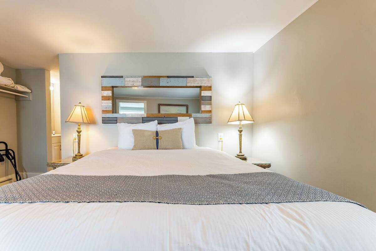 A neatly made bed with a patterned throw, two bedside lamps, and a mirror above the bed.