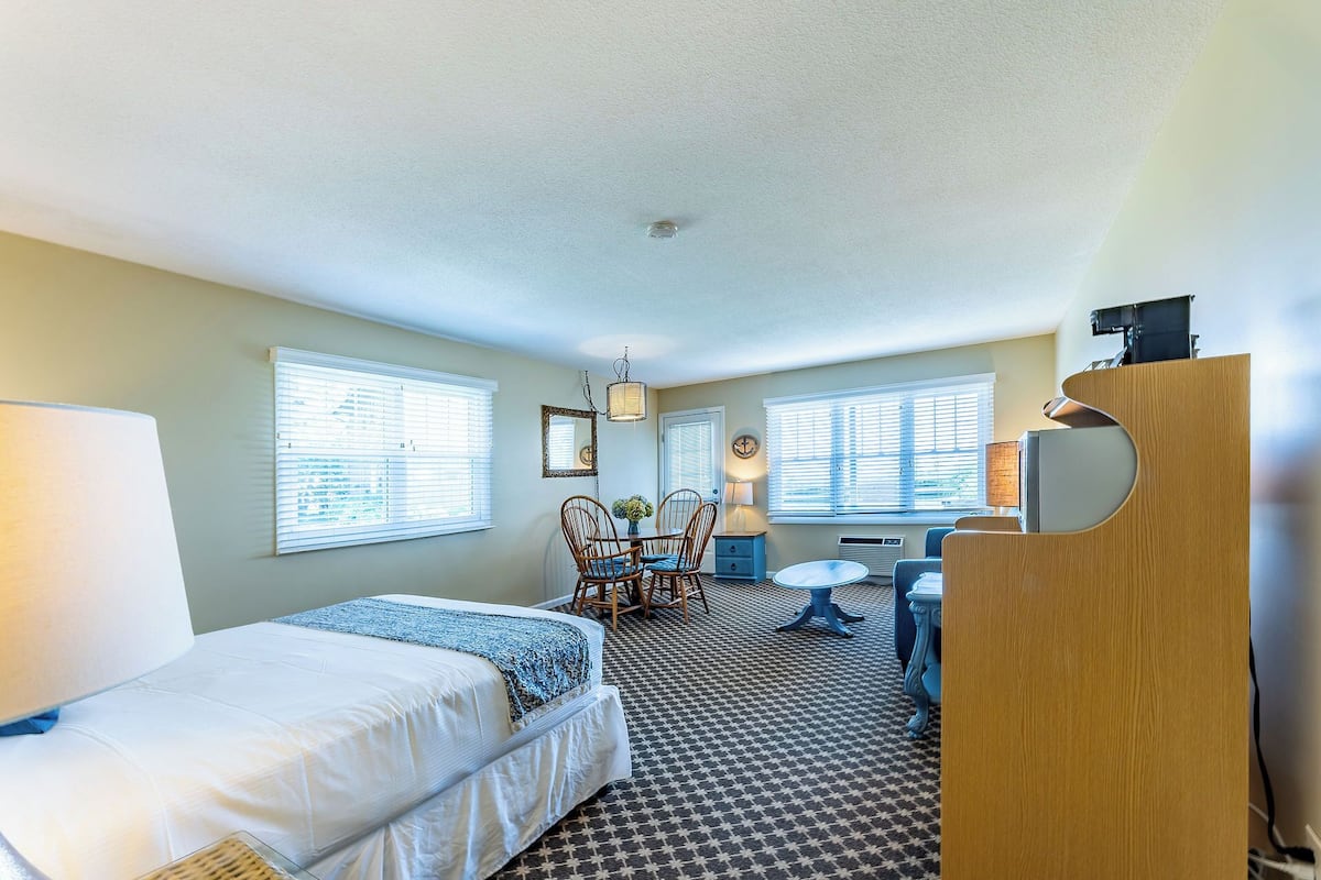 A hotel room with a bed, a desk, a chair, and a dresser.