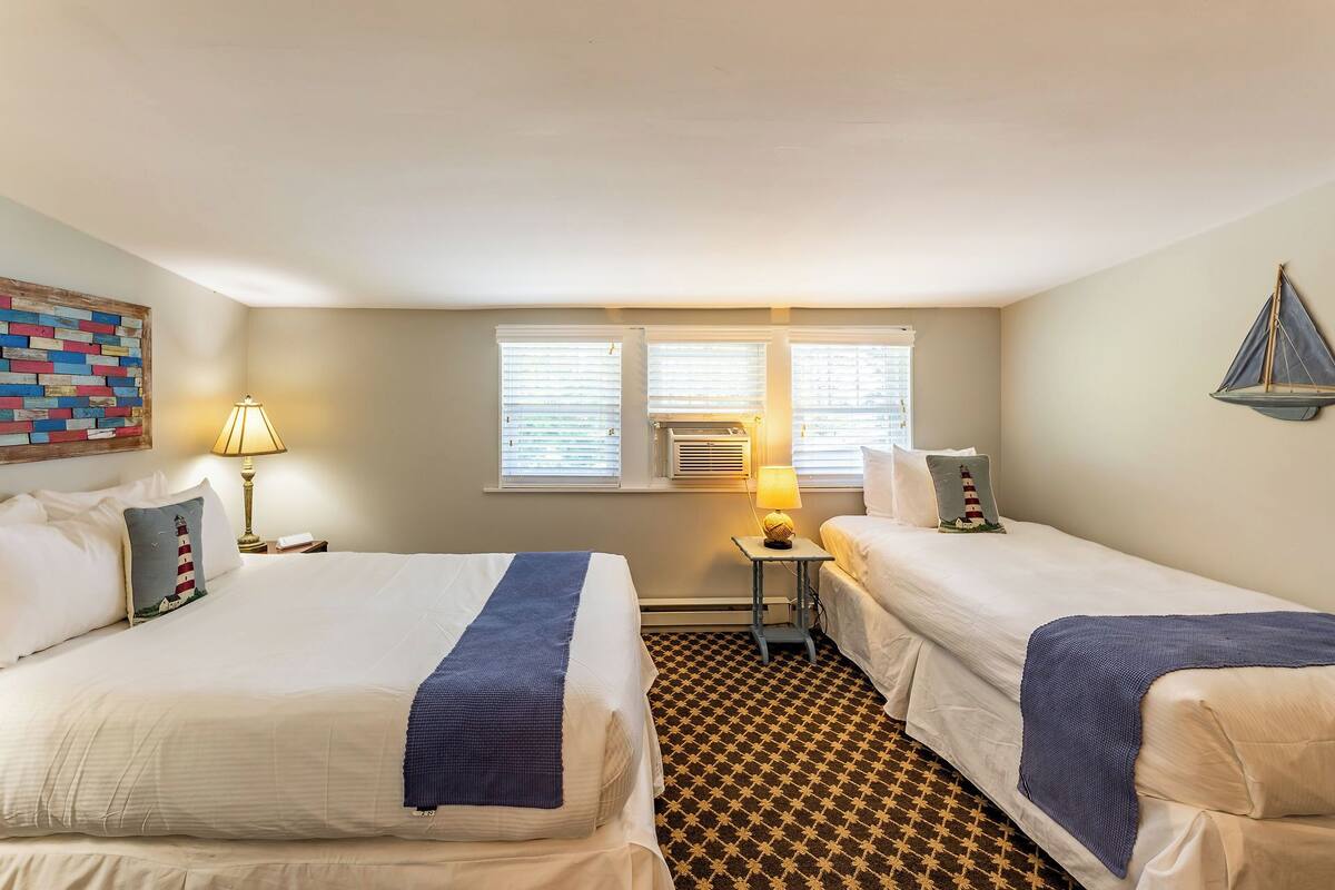 A hotel room with two beds, a patterned carpet, and a wall-mounted air conditioner.