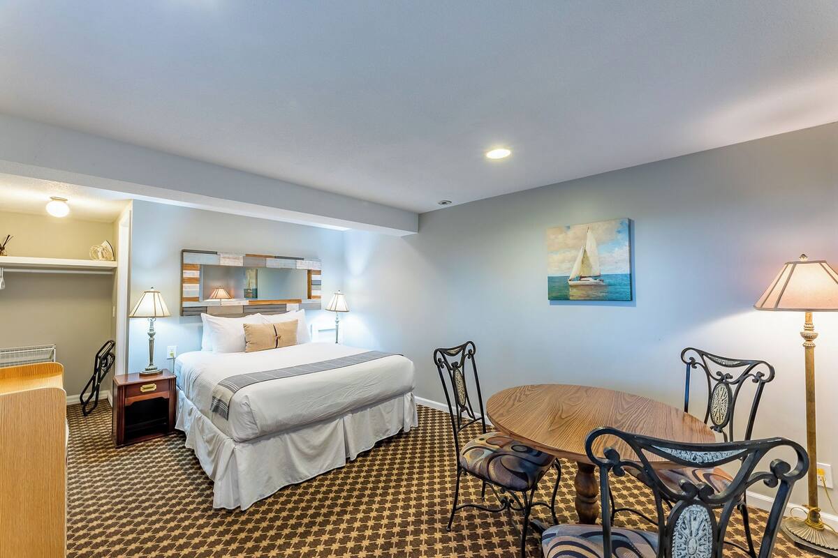 A hotel room with a bed, a desk, two chairs, a painting, and a lamp.