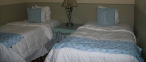 Ein Hotelzimmer mit zwei Einzelbetten, einem kleinen Tisch mit Lampe und zwei gerahmten Bildern an der Wand.