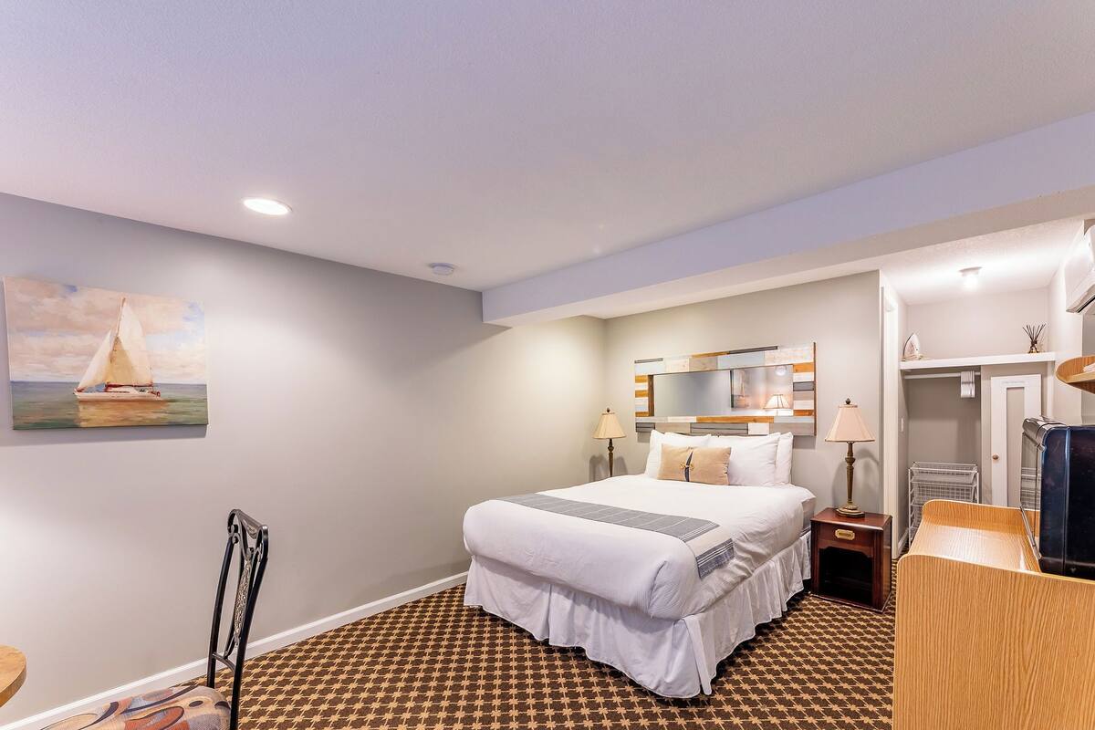A hotel room with a bed, a nightstand, a mirror, a dresser, and a painting on the wall.