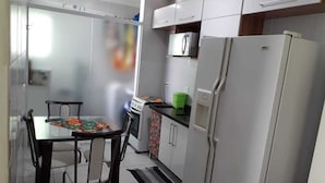 Una cocina compacta con armarios blancos, un refrigerador, un microondas y una mesa de comedor con sillas.