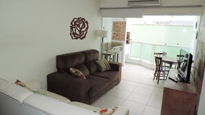 Una sala de estar con un sofá marrón, un sofá blanco, un armario de madera y un comedor con mesa y sillas.