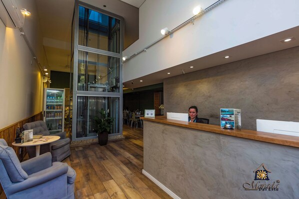A reception area with a modern design, featuring a wooden reception desk, comfortable seating, and a large glass window. - Resort Morada del Este (Canoas)