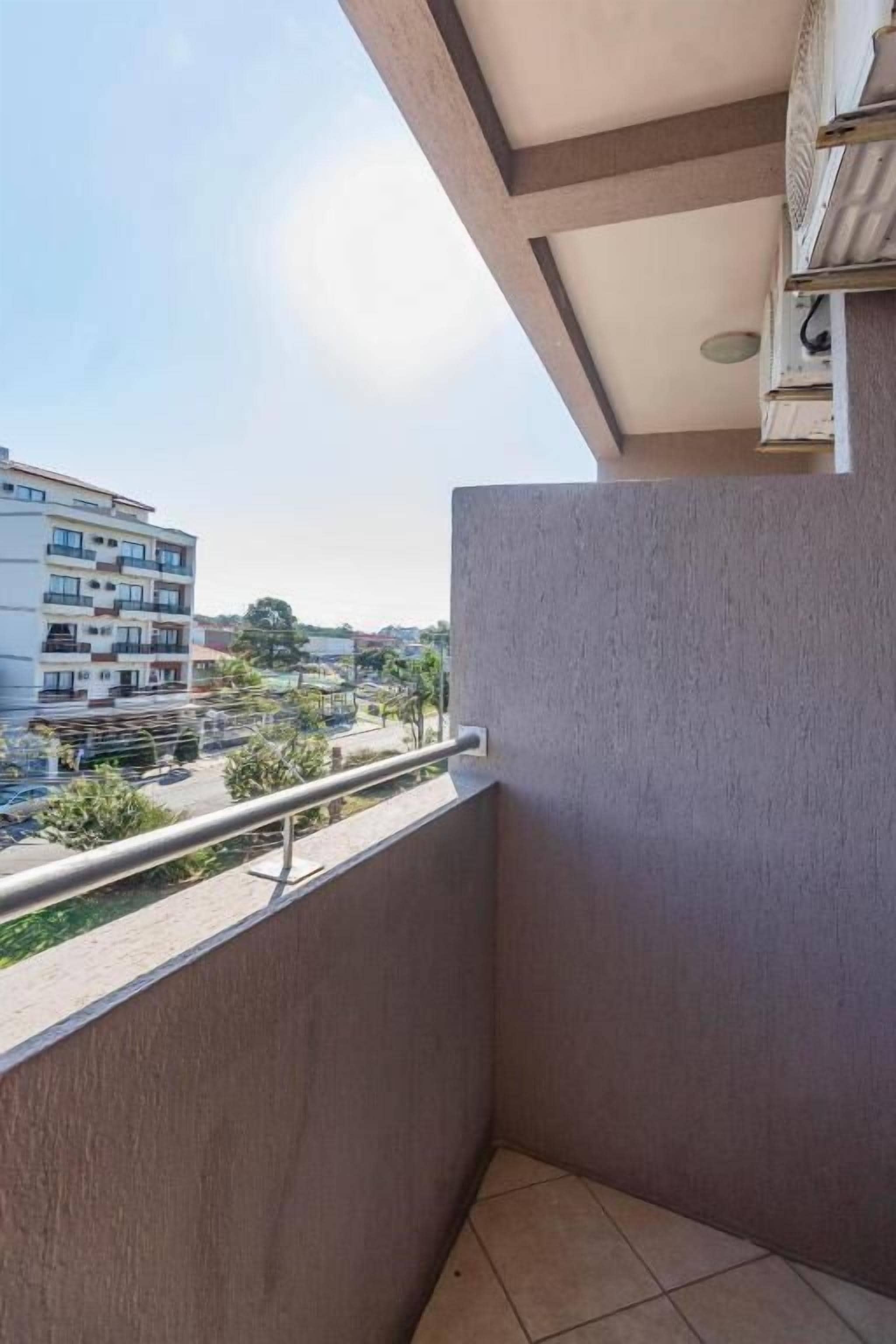 Un balcón con vista a una zona residencial, que incluye un edificio de varios pisos y un estacionamiento.