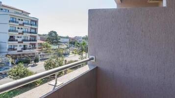 Un balcón con vista a una zona residencial, que incluye un edificio de varios pisos y un estacionamiento.