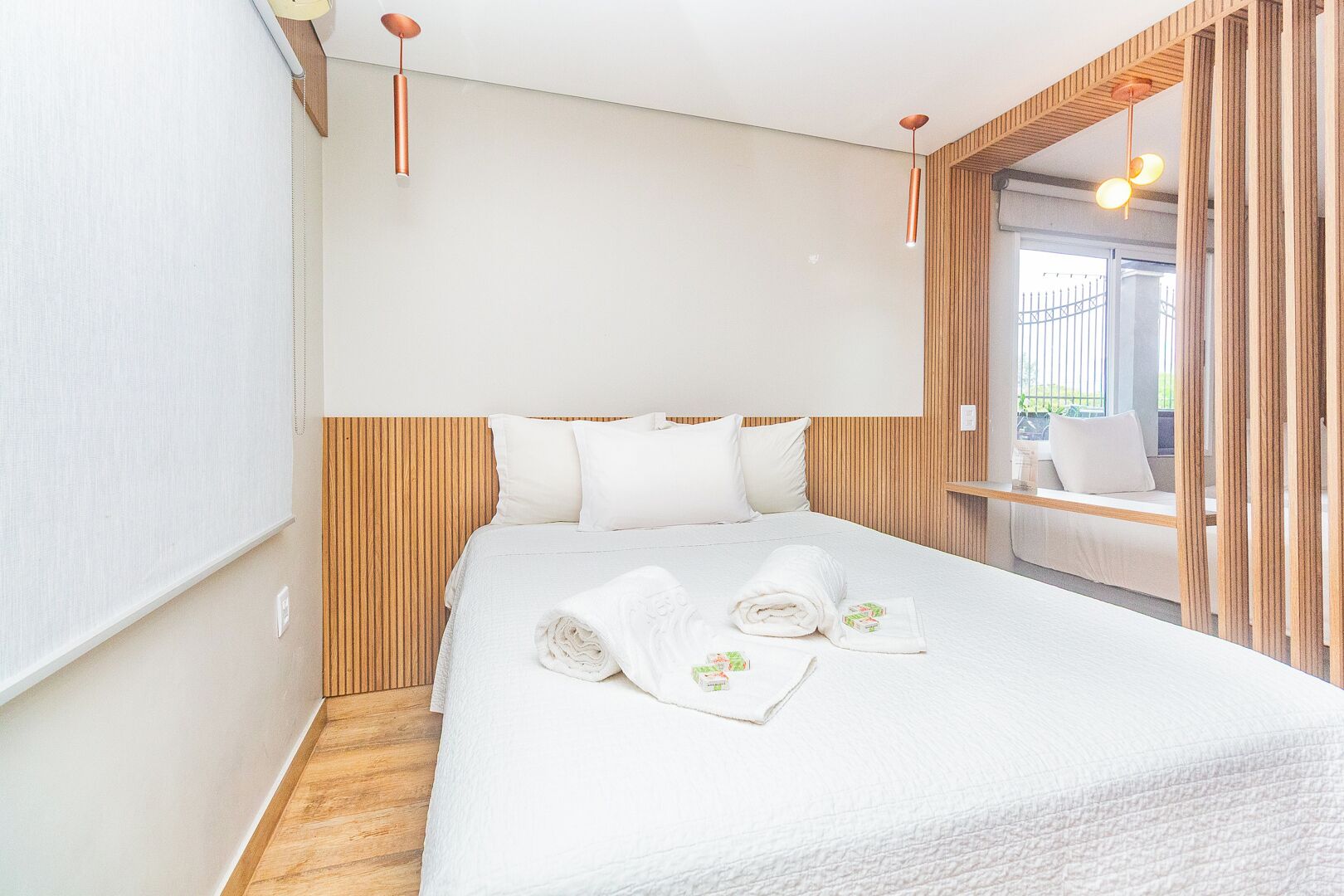 Una habitación de hotel con cama, cabecera de madera, ropa de cama blanca y dos lámparas colgantes.