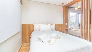 Una habitación de hotel con cama, cabecera de madera, ropa de cama blanca y dos lámparas colgantes.